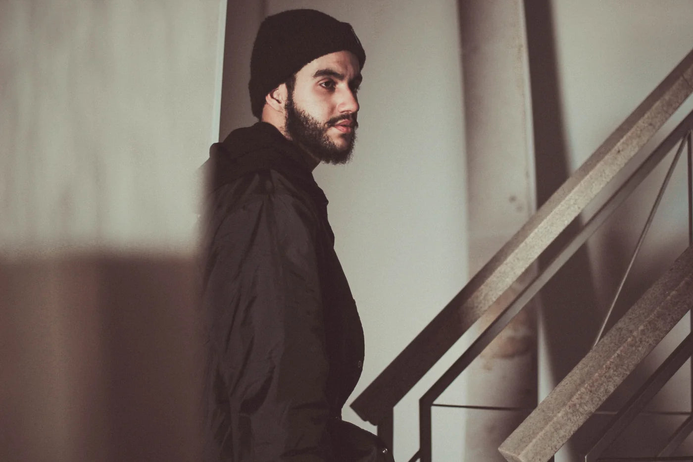 Portret van een man met een baard en zwarte muts bij een trap