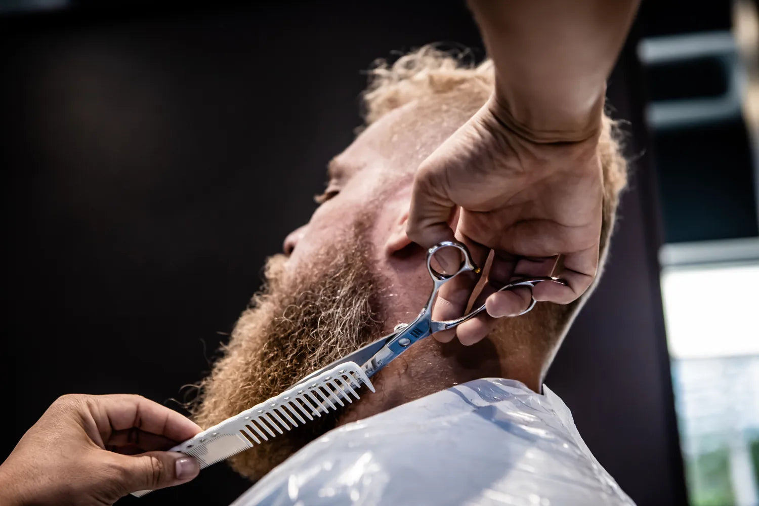 Close-up van een baard die met een kam en schaar wordt bijgewerkt